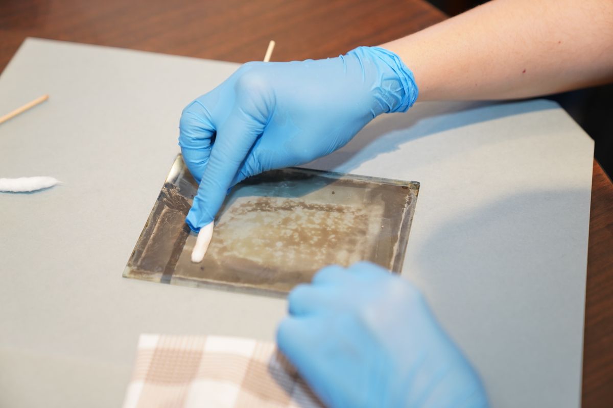 A conservator in gloves cleaning an old object